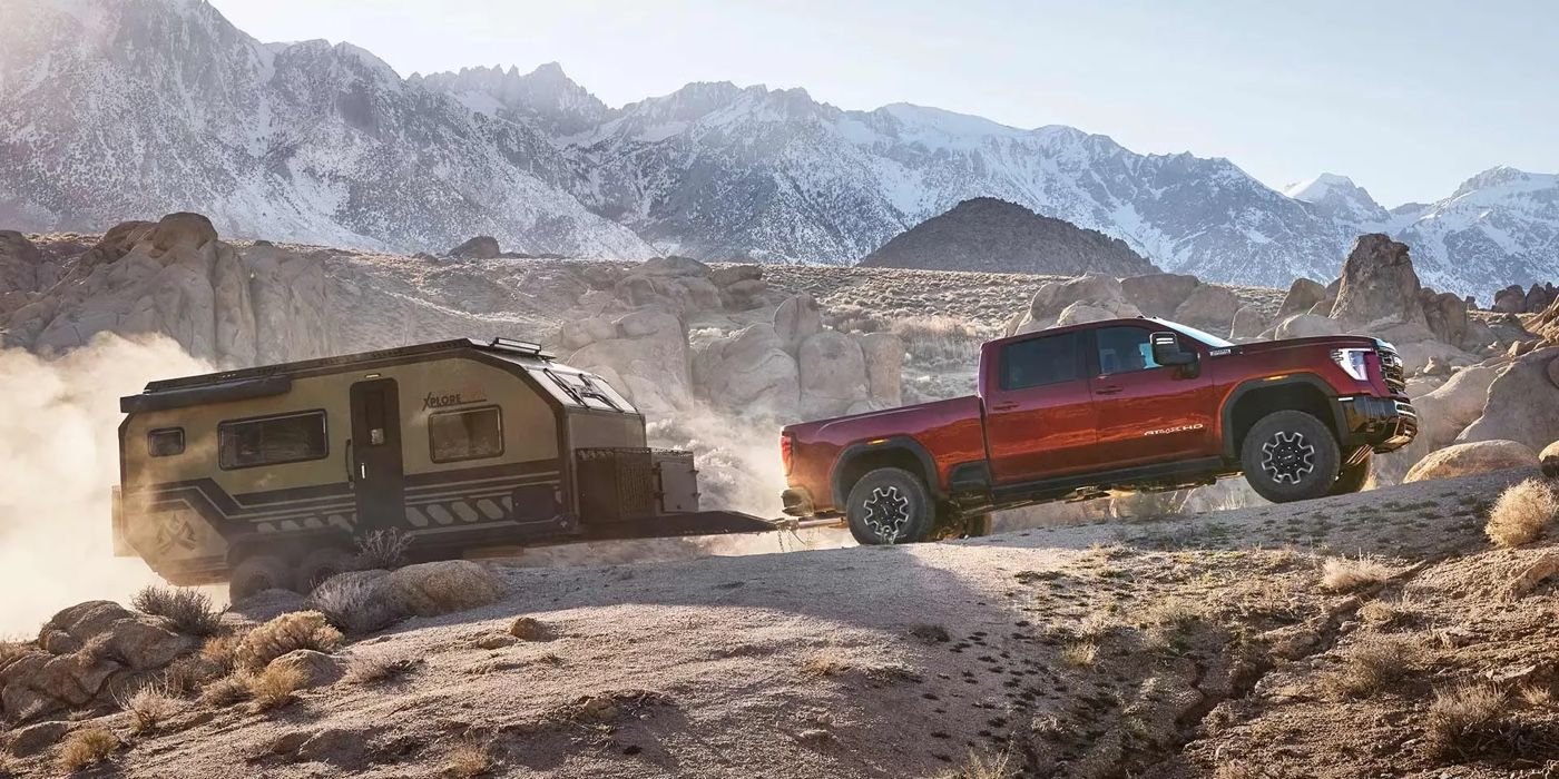 GMC Sierra HD 2026 rouge tractant une roulotte dans un paysage montagneux et poussiéreux.