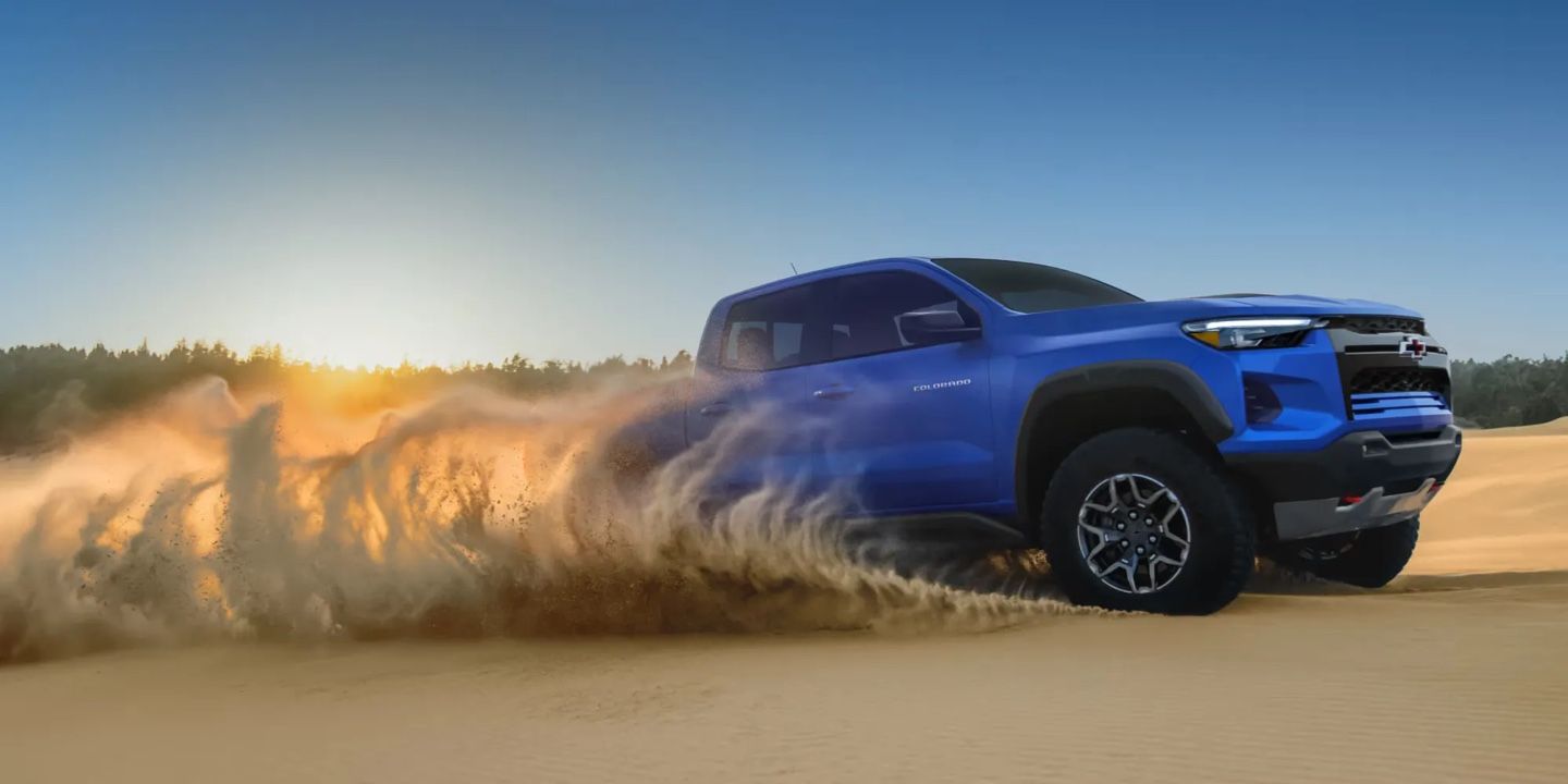 Chevrolet Colorado 2026 bleu projetant du sable en roulant dans le désert au coucher du soleil.