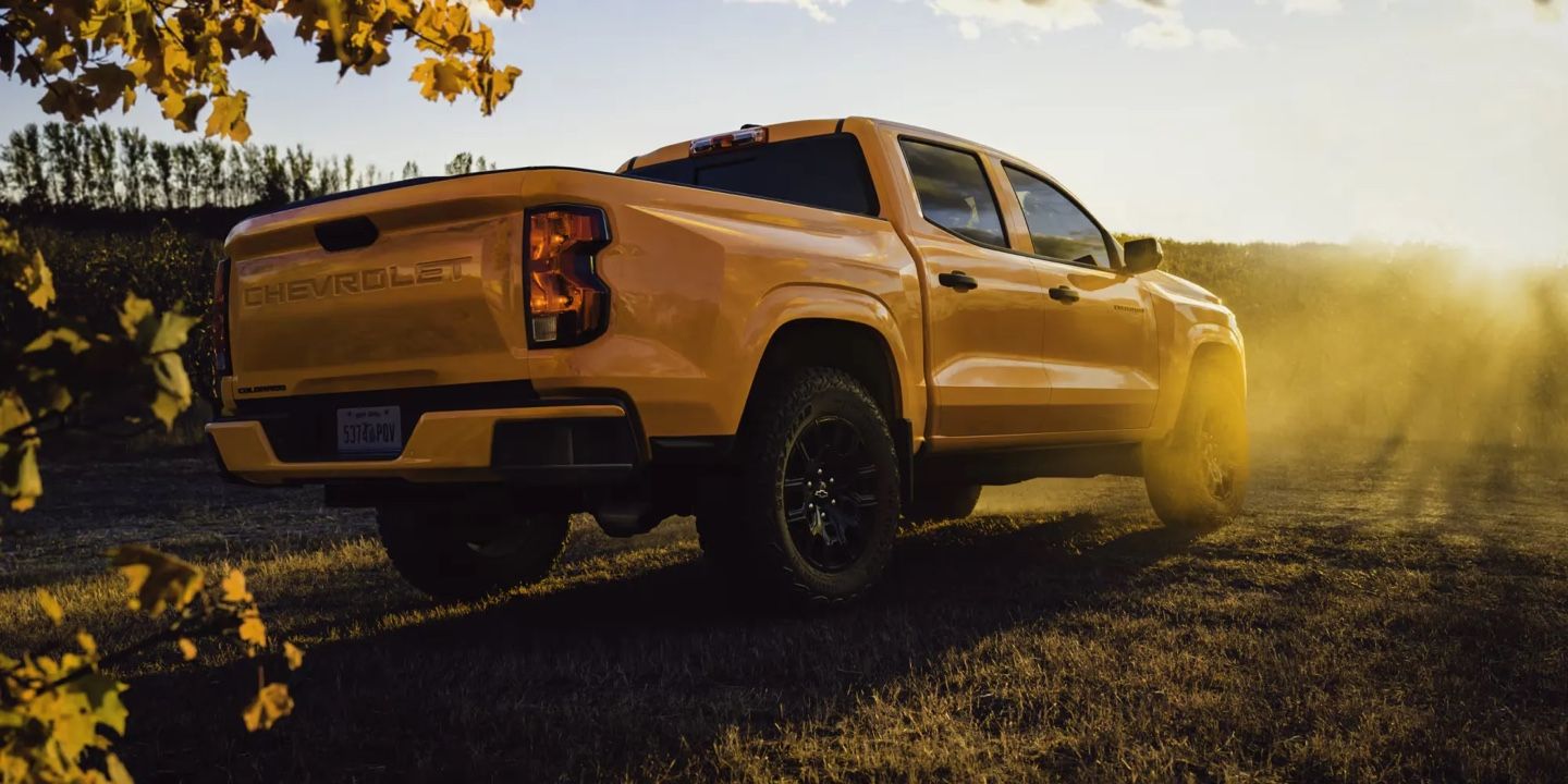 Vue arrière du Chevrolet Colorado 2026 Orange soleil circulant au coucher du soleil sur un chemin poussiéreux.