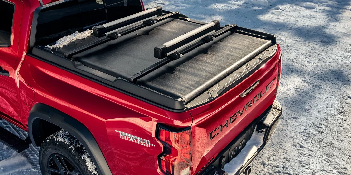 Vue du plateau arrière du Chevrolet Colorado 2026 rouge Trail Boss avec couverture rigide sur surface enneigée.