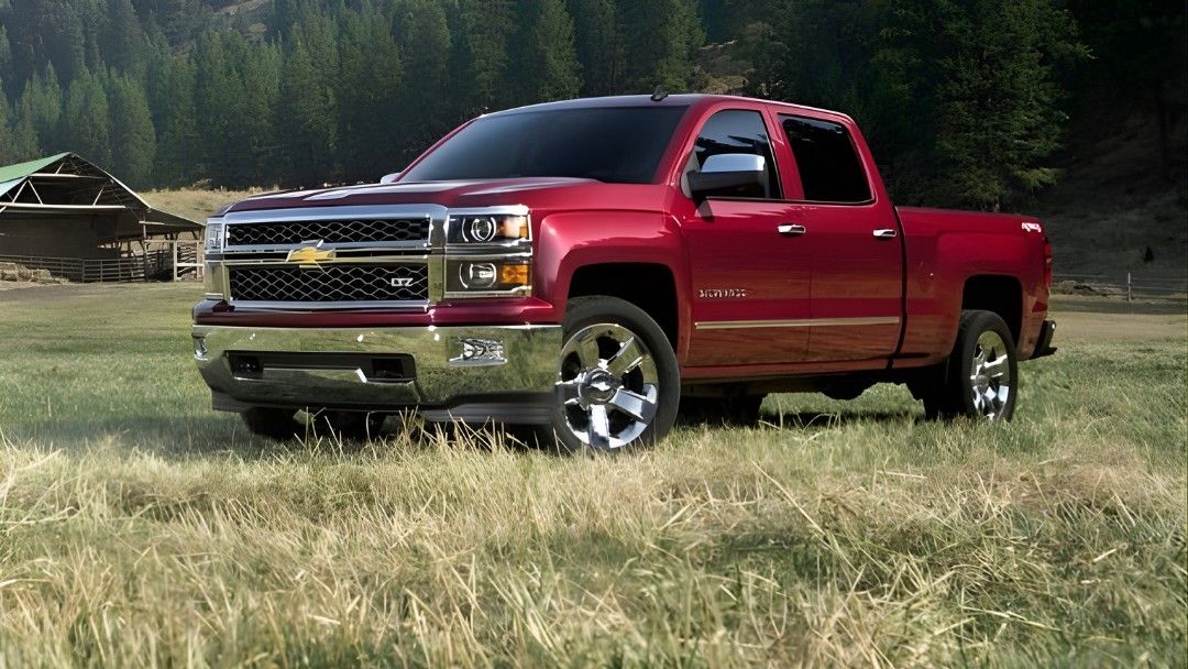 Chevrolet Silverado rouge 2014 gar&eacute; dans un champ avec une grange en arri&egrave;re-plan, repr&eacute;sentant un pickup durable et puissant.