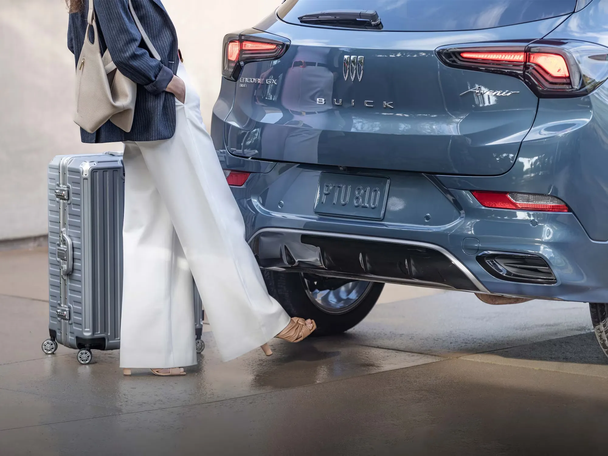 Hayon du Buick Encore GX Avenir 2026 aupr&egrave;s d&rsquo;une voyageuse avec sa valise.