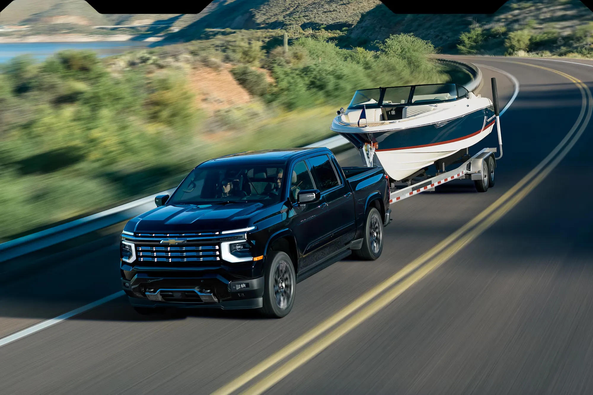 Chevrolet Silverado 1500 2027 bleu remorquant un bateau sur une route sinueuse.