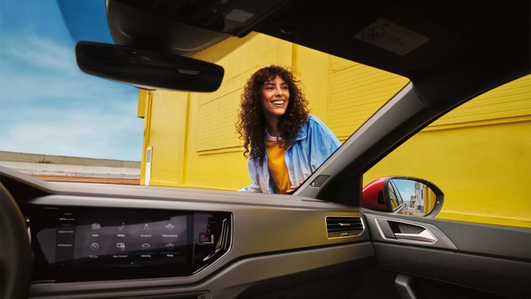 View of a smiling woman from inside a Volkswagen.
