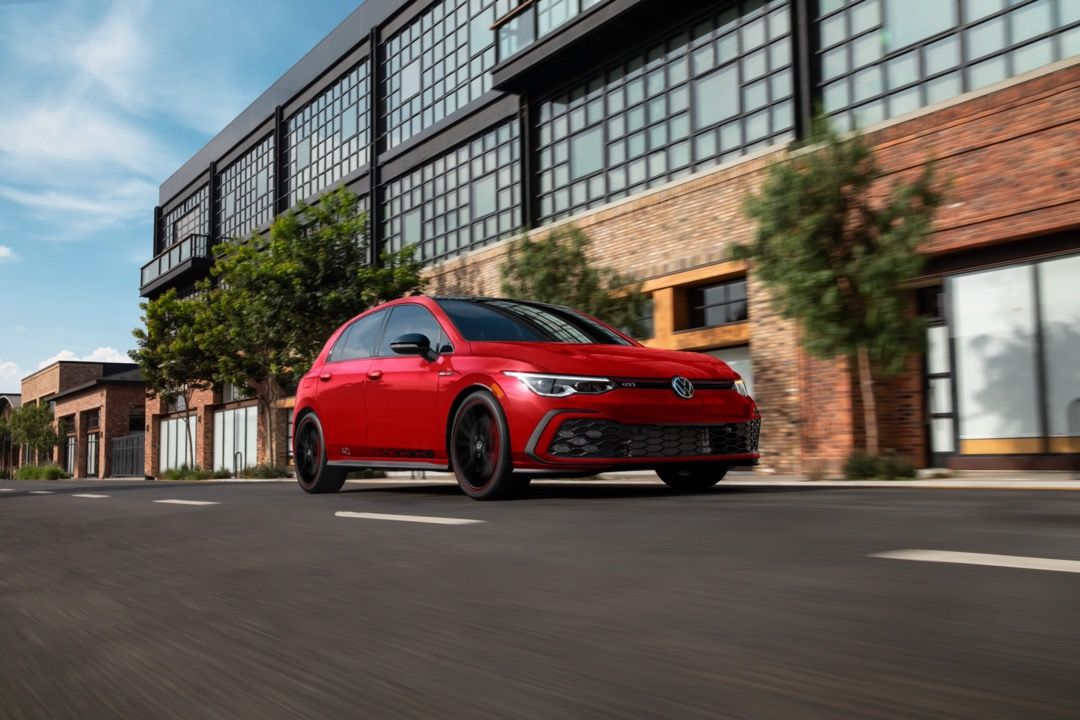 Front 3/4 view of the 2023 Volkswagen Golf GTI driving on a road.