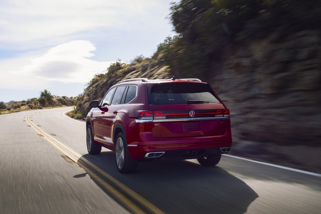 Rear 3/4 view of the 2024 Volkswagen Atlas driving on a road.