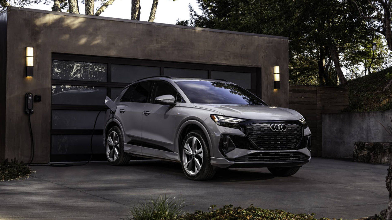 front side view of a 2025 Audi Q4 e-tron plugged to a charging station in front of a garage