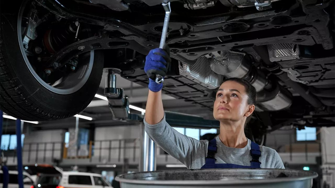Technicienne inspectant les composants sous la carrosserie d’un véhicule Volkswagen, illustrant la précision technique de la plateforme MQB utilisée par les Golf GTI et Golf R 2026.