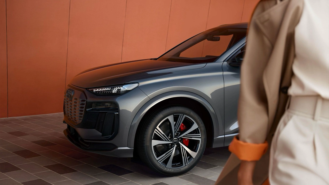 Version SQ6 de l&rsquo;Audi Q6 e-tron stationn&eacute;e devant un mur orang&eacute; pour illustrer les prix et versions.