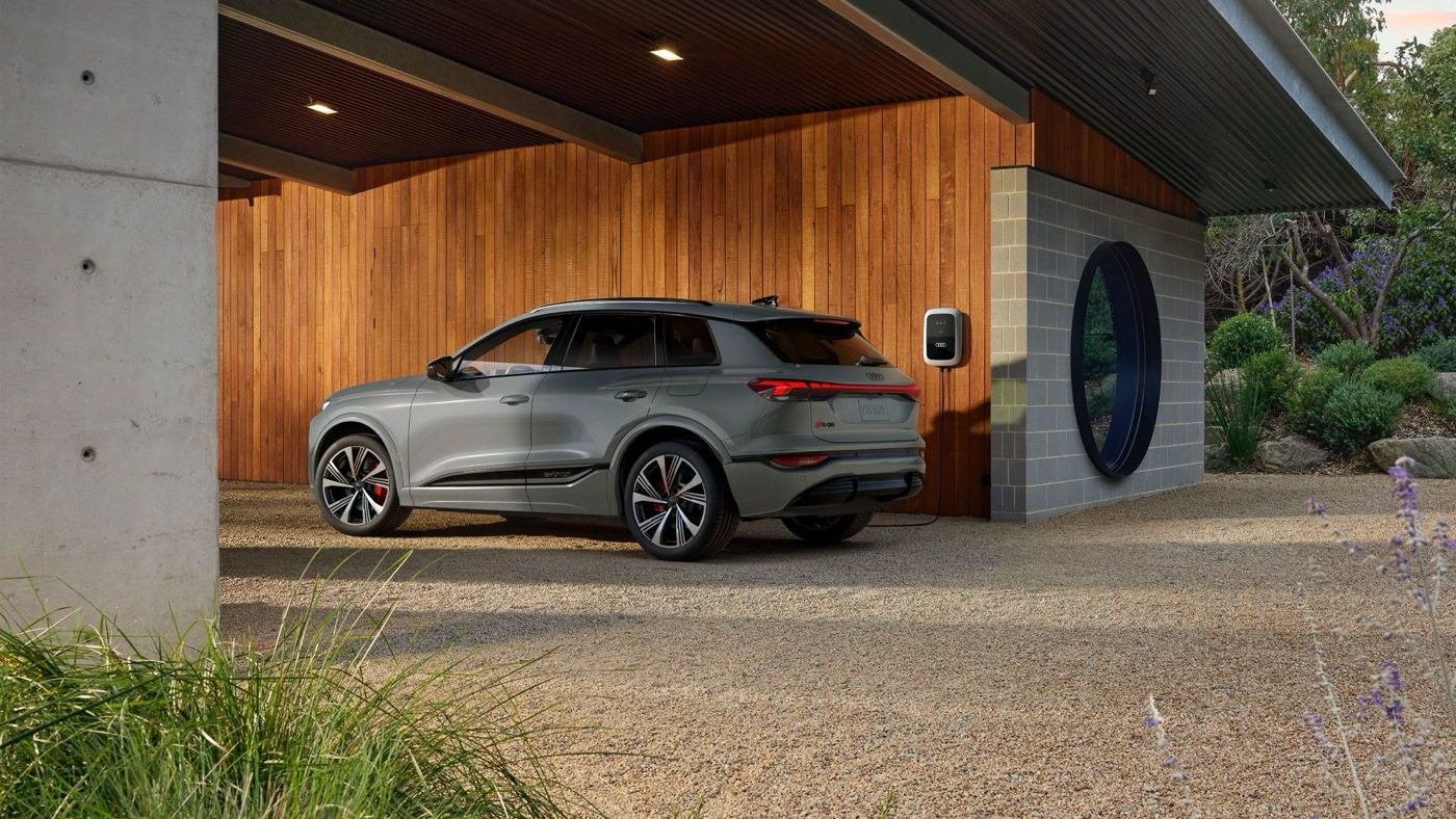 Version SQ6 gar&eacute;e devant une r&eacute;sidence avec borne de recharge pour illustrer l&rsquo;autonomie de la batterie.