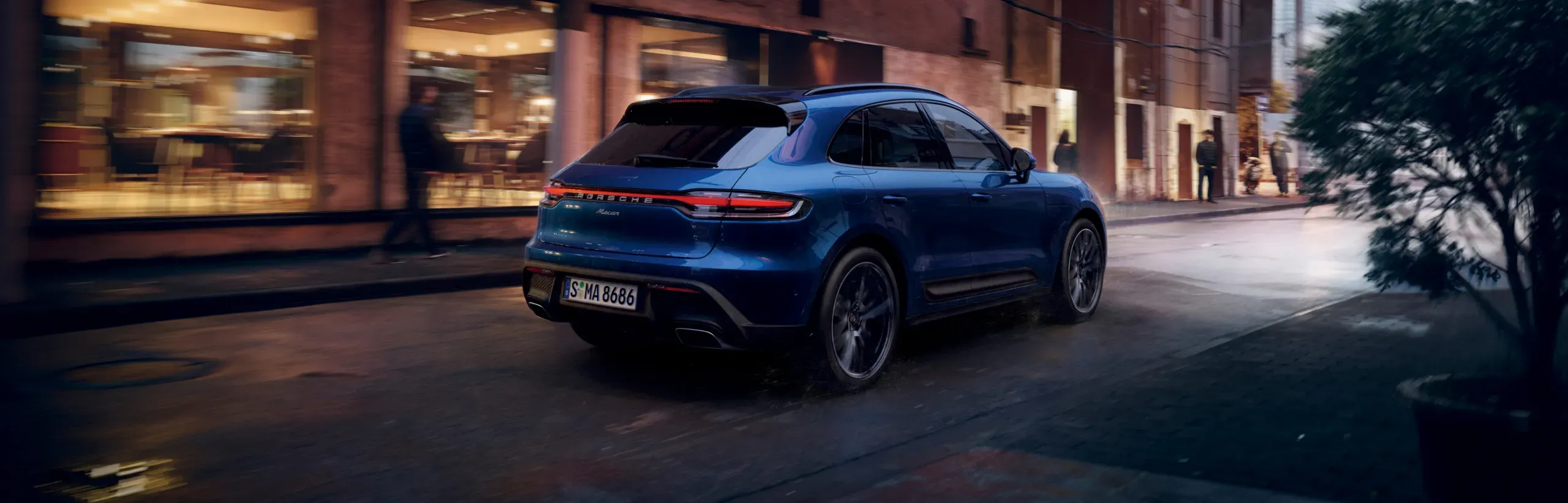 Blue 2026 gas Porsche Macan seen from the rear in the city to illustrate the specifications and powertrains.