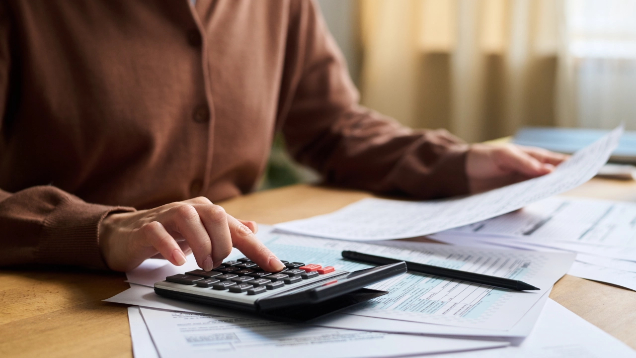 Close-up of a hand using a calculator next to automotive documents