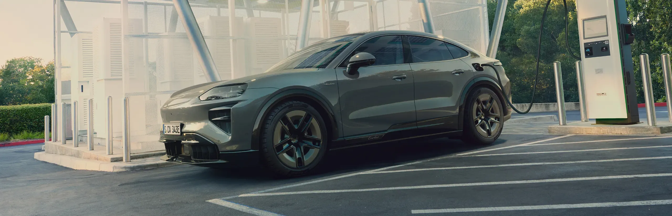 2027 Porsche Cayenne electric coupe parked at a charging station, viewed from a front three-quarter angle.