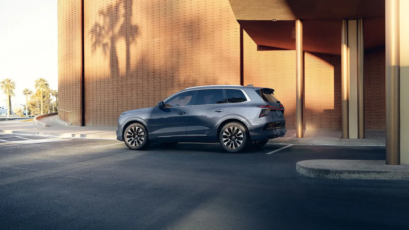 Blue 2027 Audi Q7 viewed from the side and rear three-quarter angle in front of a gold-toned building.