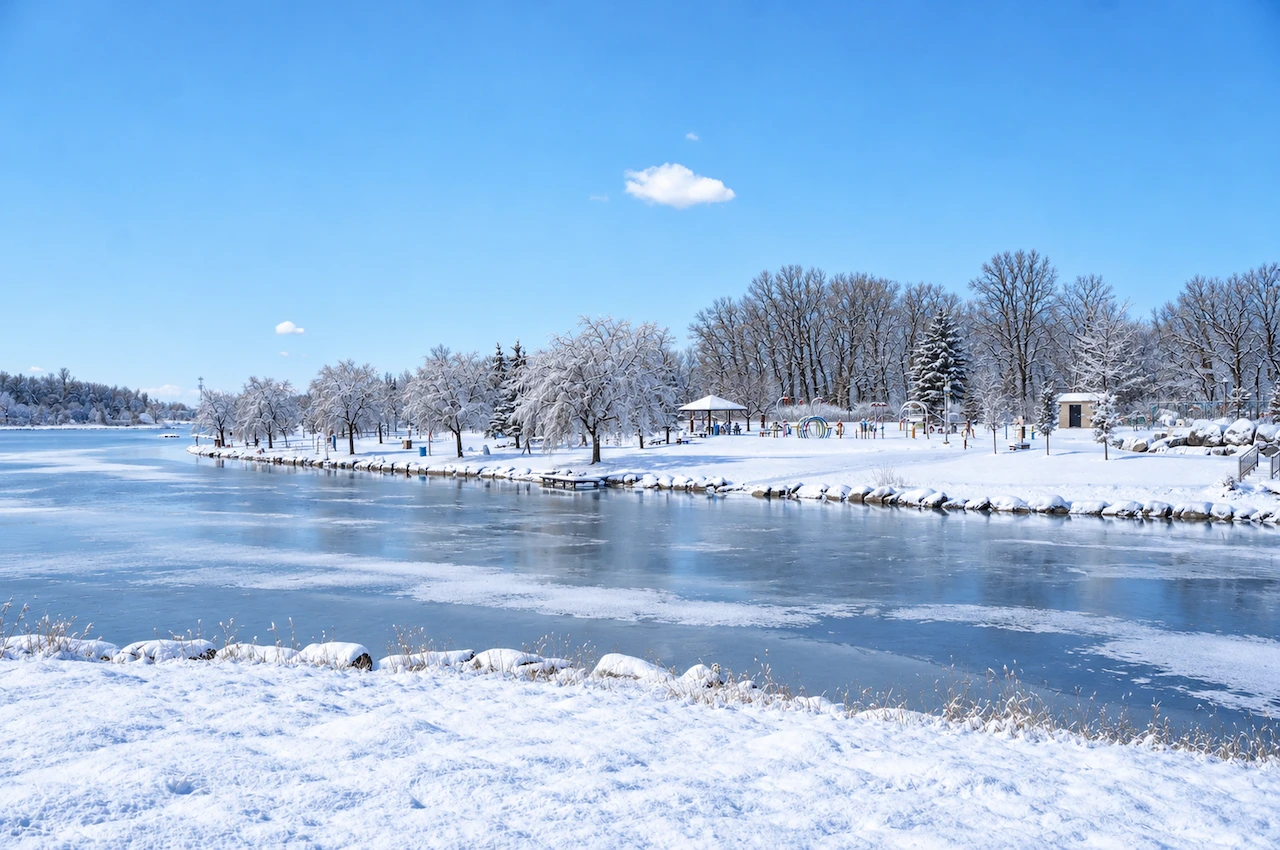 Étendue d’eau gelée bordée d’arbres enneigés pour une promenade hivernale au parc de la Cité à Saint-Hubert.
