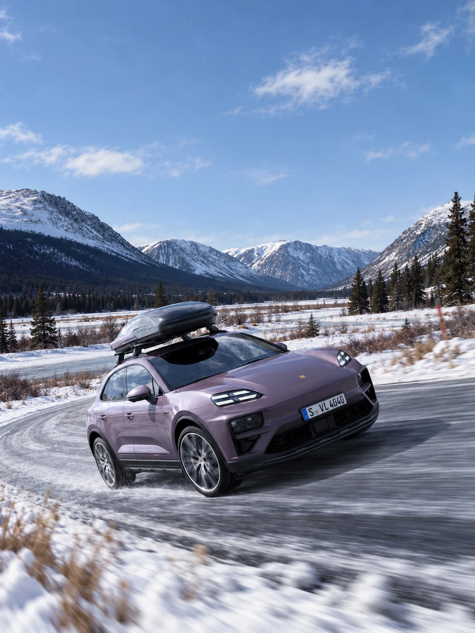 Porsche Macan 4 &eacute;lectrique 2024 avec coffre de toit sur une route de montagne en hiver.
