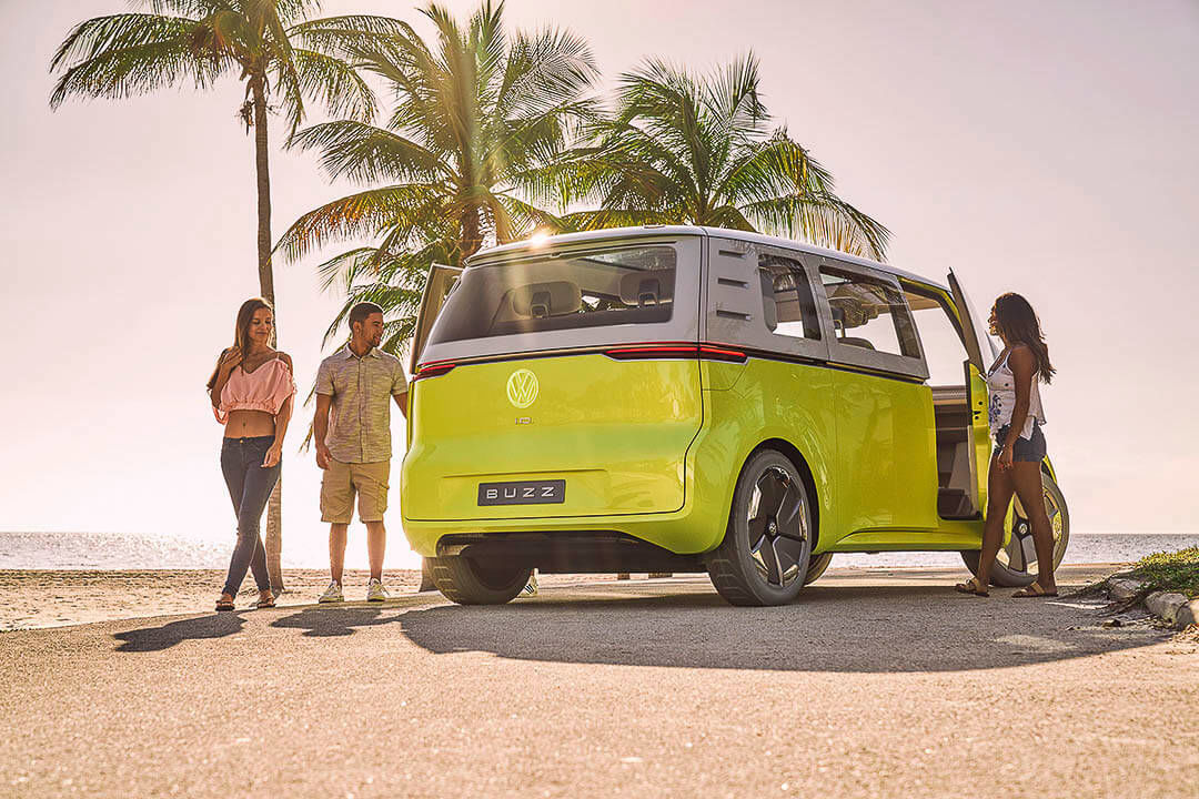 Groupe d'amis sortant d'un VW Westfalia électrique garé à côté de palmiers sur une plage