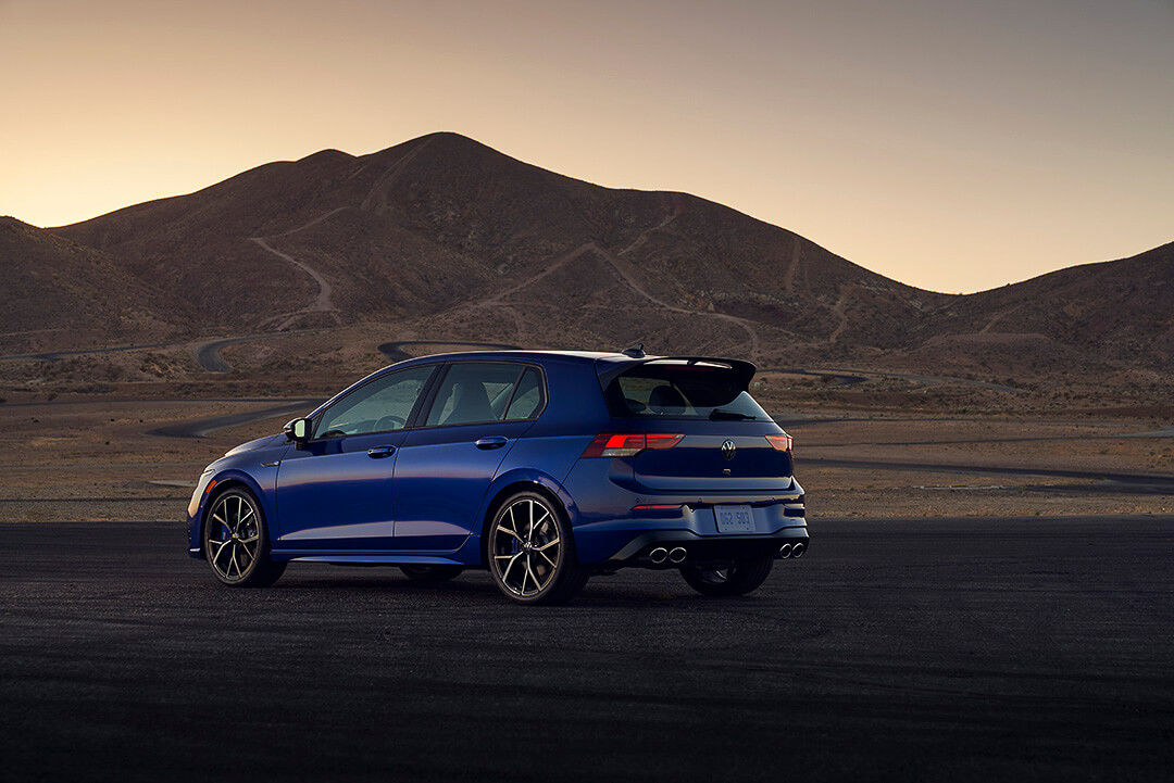 Rear 3/4 side view of a 2022 Golf R parked outdoors with a mountain in the distance
