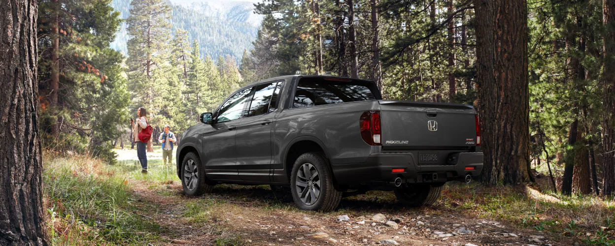 rear side view of a 2023 Honda Ridgeline on a trail with two hikers