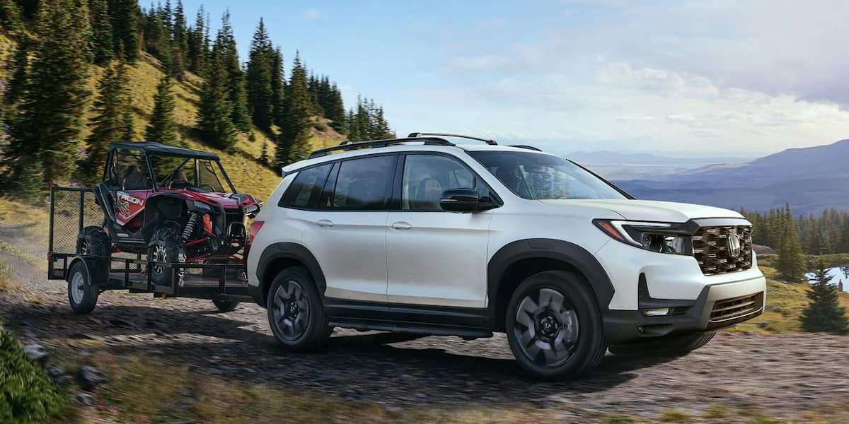 front side view of a 2023 Honda Passport pulling a trailer with a ATV on it in the forest