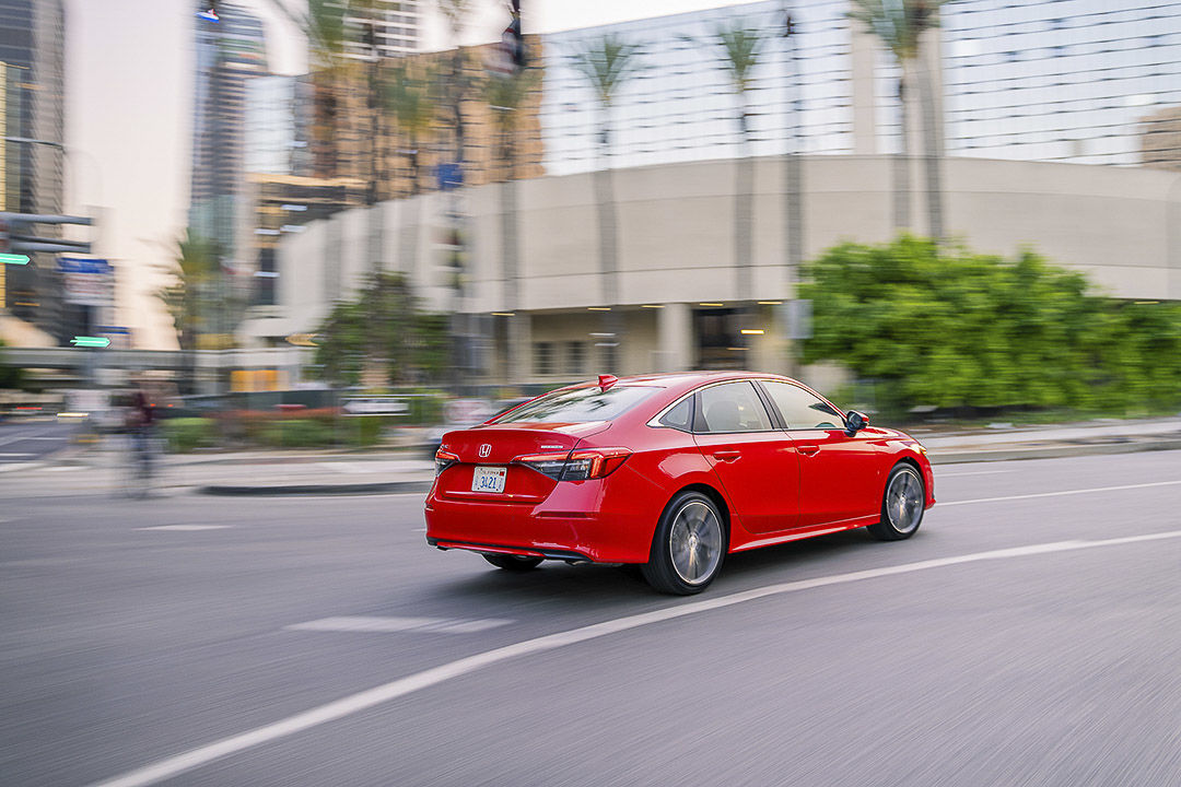Side-rear view of red 2022 Honda Civic Touring making a turn on a city boulevard
