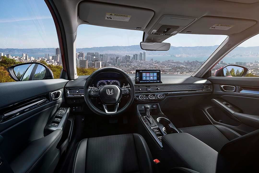 Front interior of a 2022 Honda Civic Touring including all its technologies with a large city in the distance