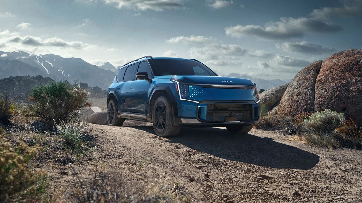 VUS électrique Kia bleu sur une route de gravier, illustrant la préparation d’un achat au printemps avant la haute saison.