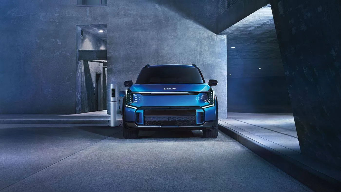 Kia EV9 2026 bleu à une borne de recharge, un VUS électrique à trois rangées adapté aux familles.