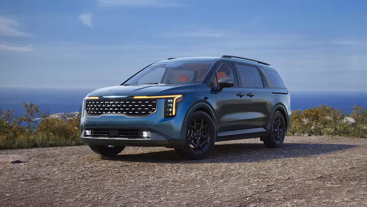 Kia Carnival 2026 vert fonc&eacute; stationn&eacute; sur un belv&eacute;d&egrave;re de gravier au bord de la mer, avec jantes noires