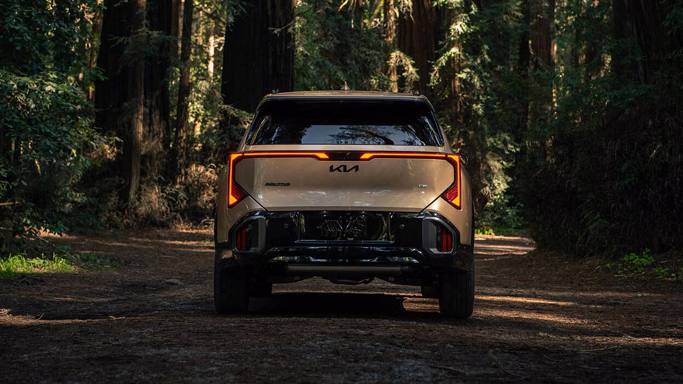 Kia Seltos 2027 beige vu de l'arri&egrave;re sur un chemin forestier