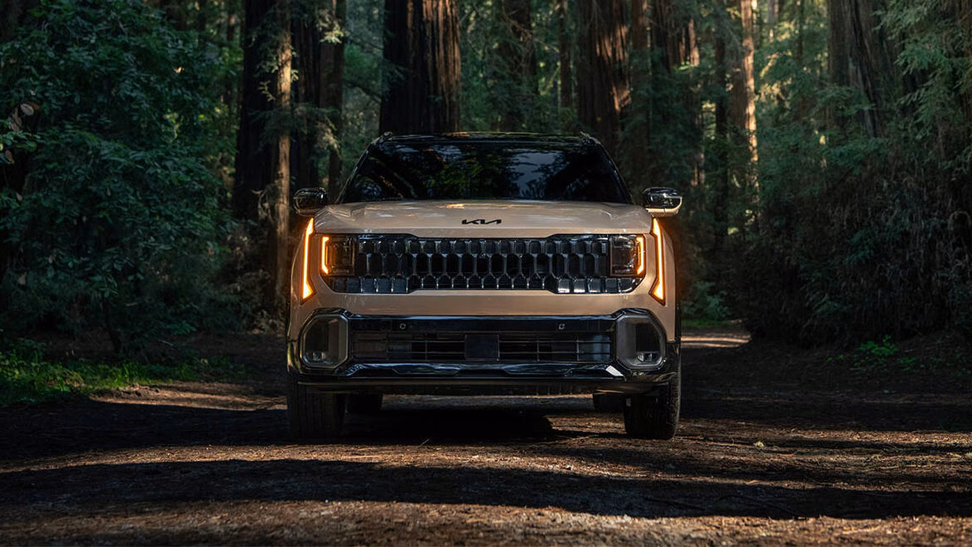 Kia Seltos 2027 beige vu de face sur un chemin forestier, phares allum&eacute;s