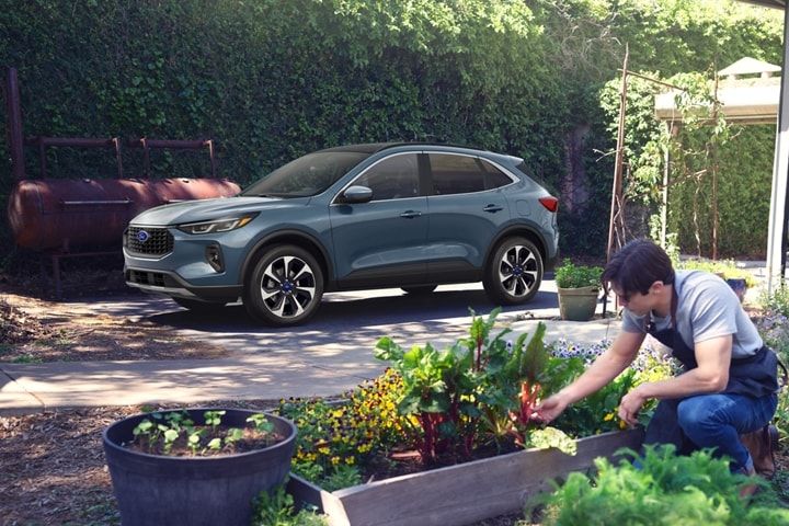 Un mpnsieur jardine pendant que son Ford escape est stationné dans son allée.