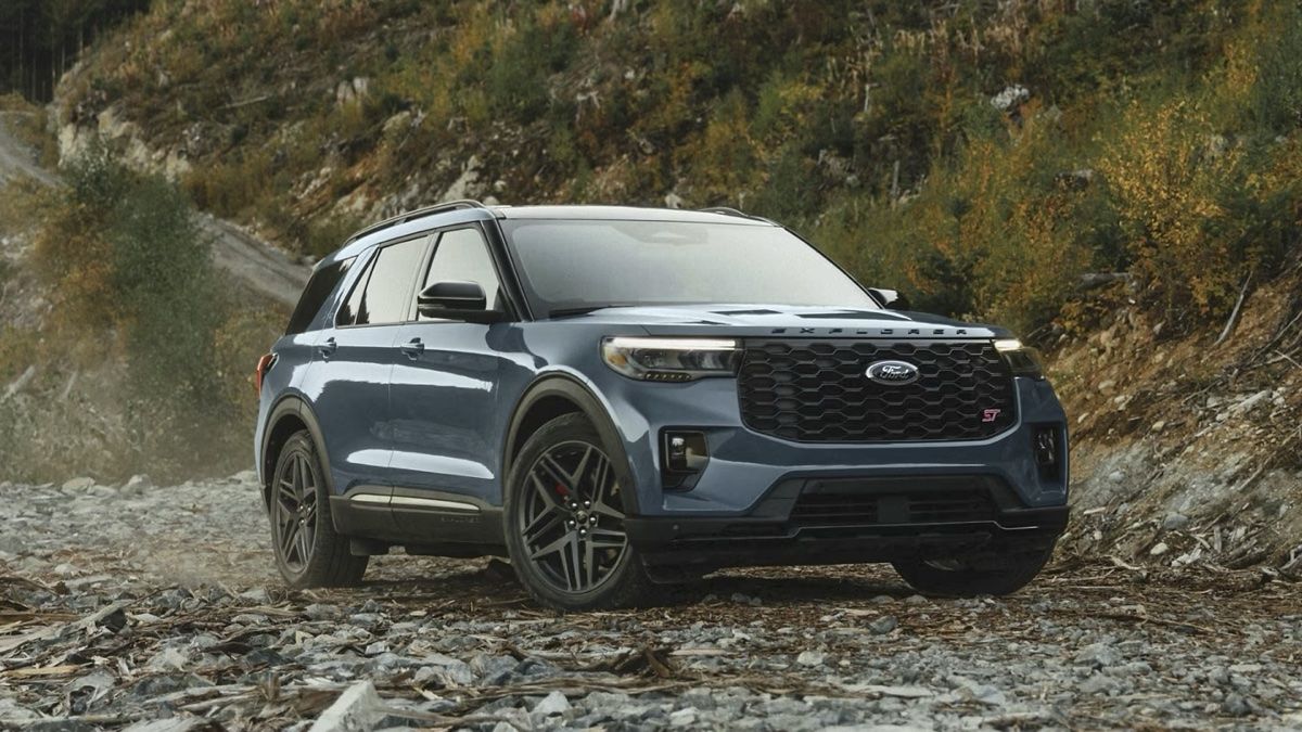 Présentation du Ford Explorer ST 2025 stationné sur la gravel au bord d'une forêt.