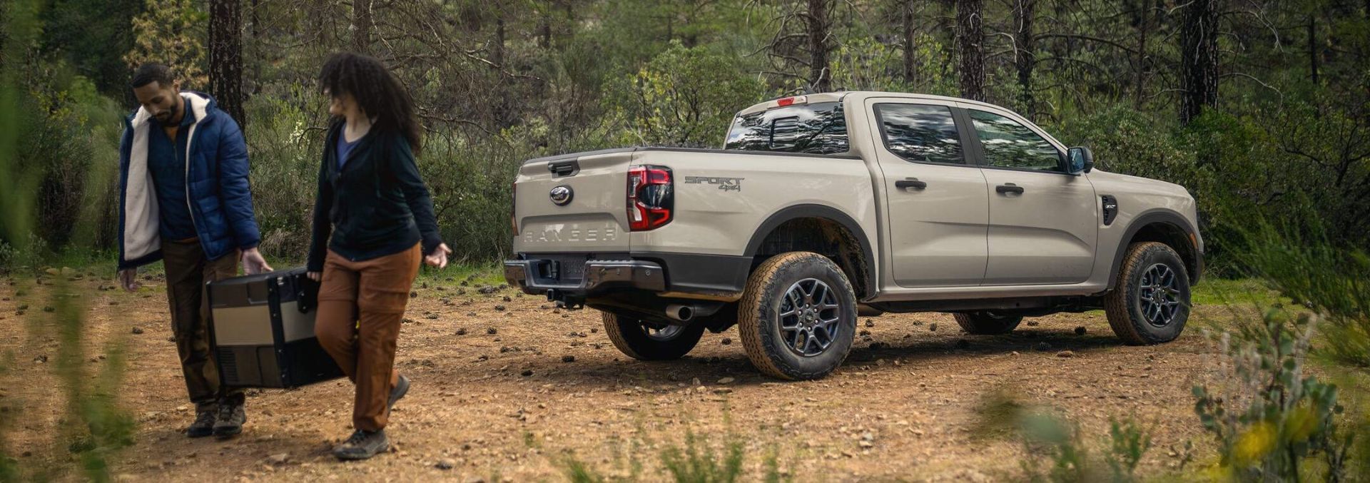 vue latérale arrière d'un Ford Ranger 2025 en forêt à cote de ses deux conducteurs