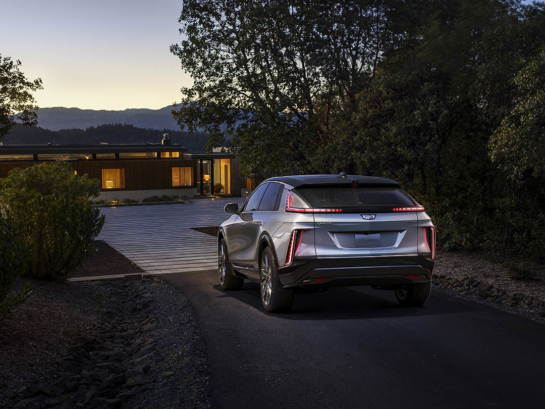 Rear 3/4 view of the 2023 Cadillac Lyriq parked behind a house.