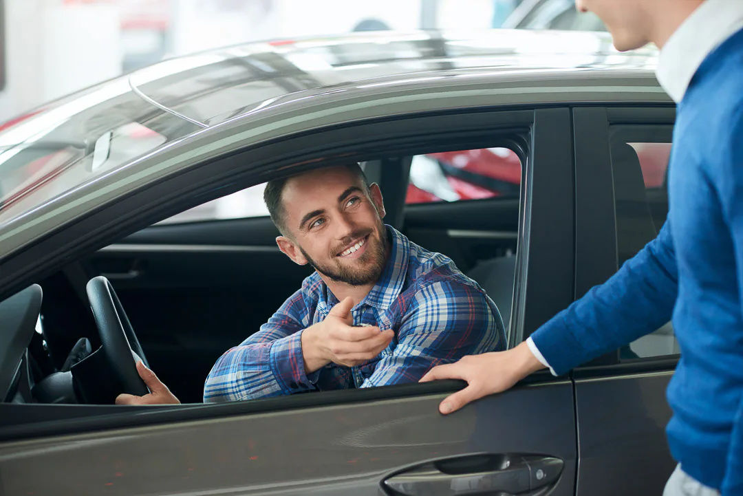 young man sitting in a car in a dealership, talking to the sales representative