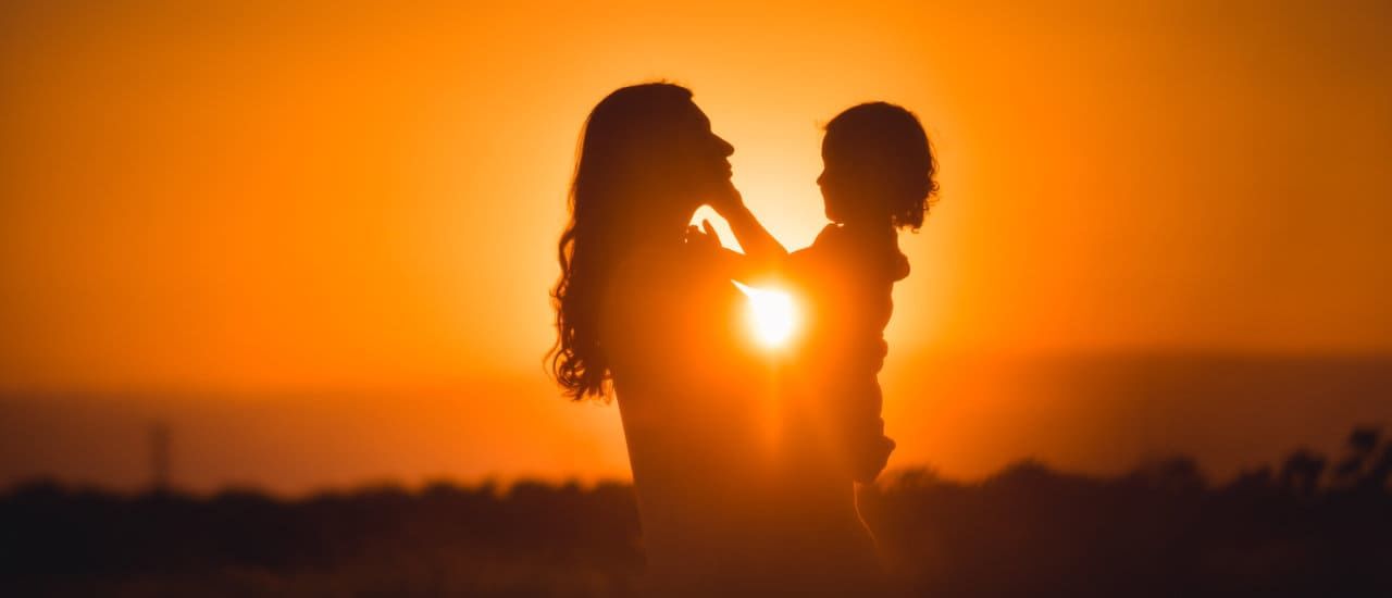 silhouette of a woman and her child in front of a sunset