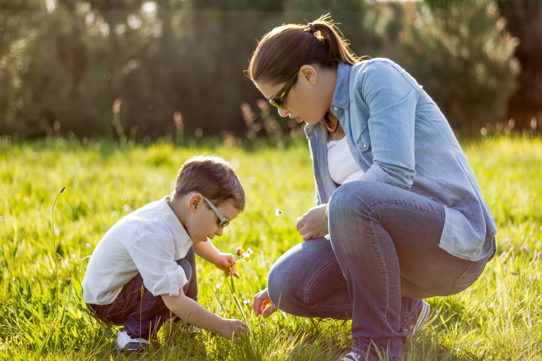 Mère et fils cueillant des fleurs dans un champ ensoleillé.