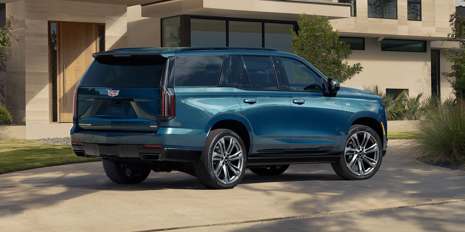 Vue 3/4 arrière du Cadillac Escalade 2025 garé dans une cours d'une maison.