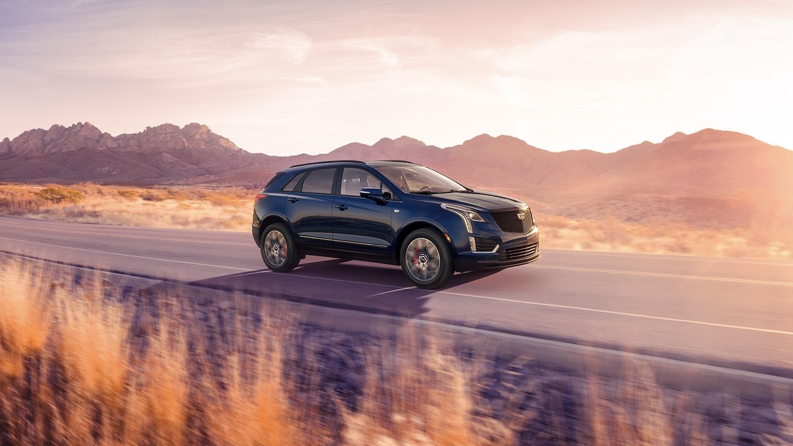 Cadillac XT5 driving on a road with a mountain range and rising sun in the background