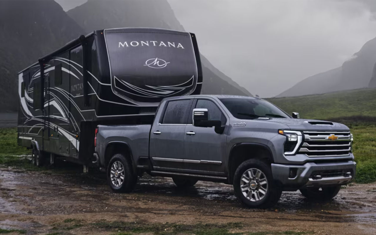 vue latérale avant d'une Chevrolet Silverado High Country 2024 remorquant une roulotte de type '5th wheel' dans une vallée brumeuse