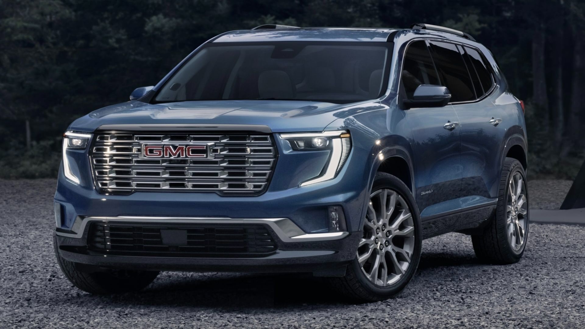 Un GMC Acadia stationné sur de la gravel au bord d'un bois.