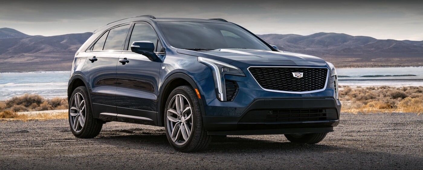 Blue 2021 Cadillac XT4 parked by the sea with mountains in the distance