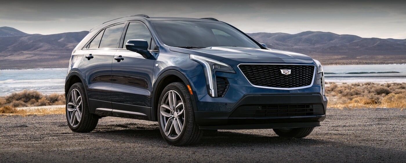 Le Cadillac XT4 2021 bleu garé au bord de la mer avec les montagnes au loin