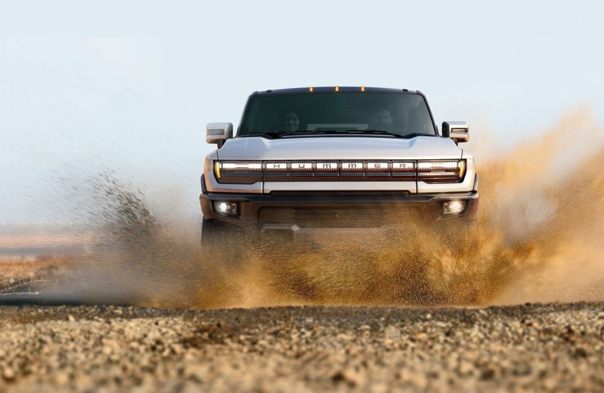 Vue avant du GMC Hummer EV 2023 blanc éclaboussant l'eau en traversant une marre