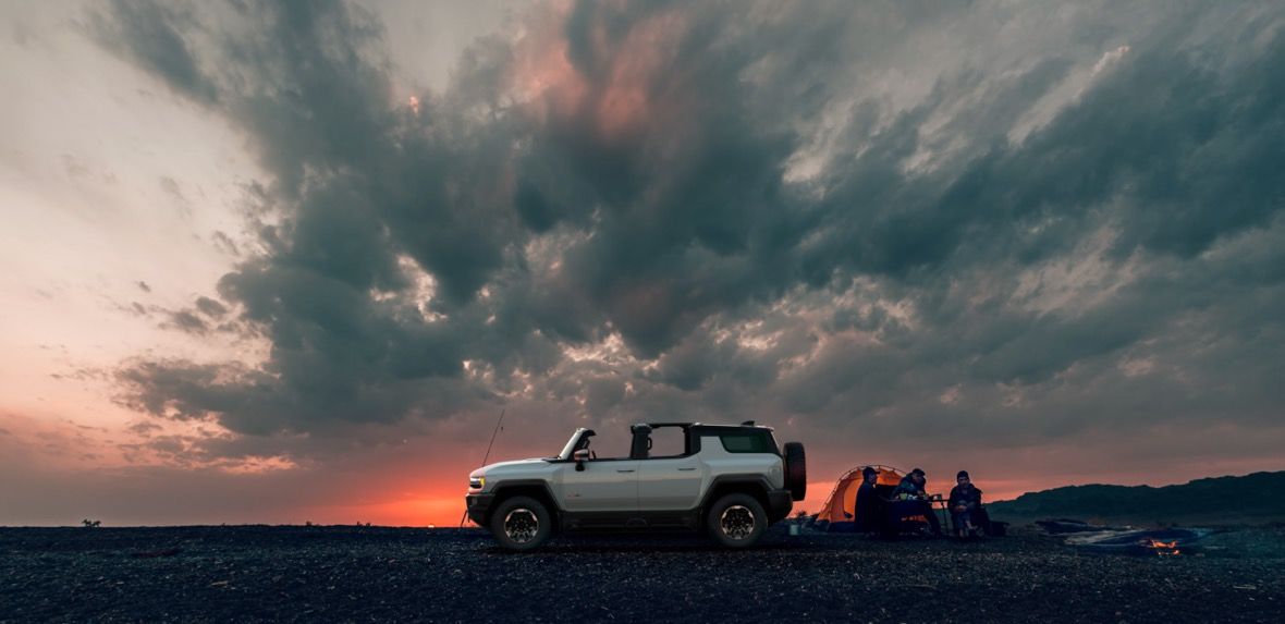 Vue latérale du pickup Hummer EV 2024 blanc garé sur une terre incluant trois personnes en camping sauvage