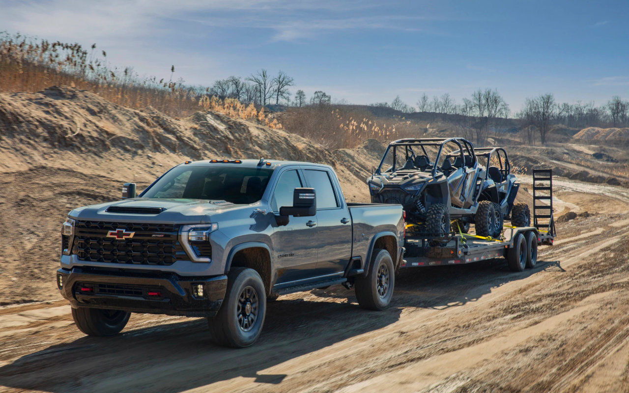 vue latérale avant d'un camion Chevrolet Silverado HD 2023 remorquant des VTT sur une route de sable