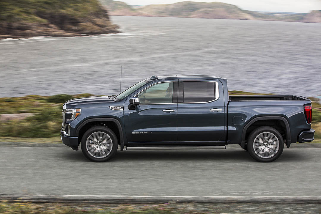 Vue latérale du GMC Sierra 1500 Denali 2021 bleu roulant sur la route longeant une mer