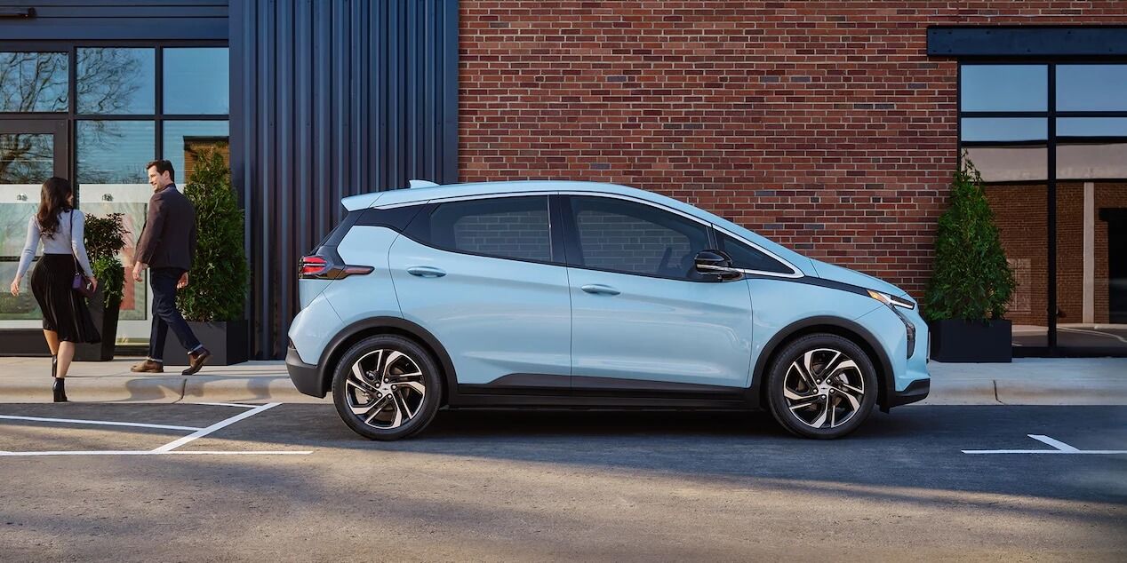 Un couple se dirigeant dans un immeuble incluant la vue latérale de la Chevrolet Bolt EV 2021