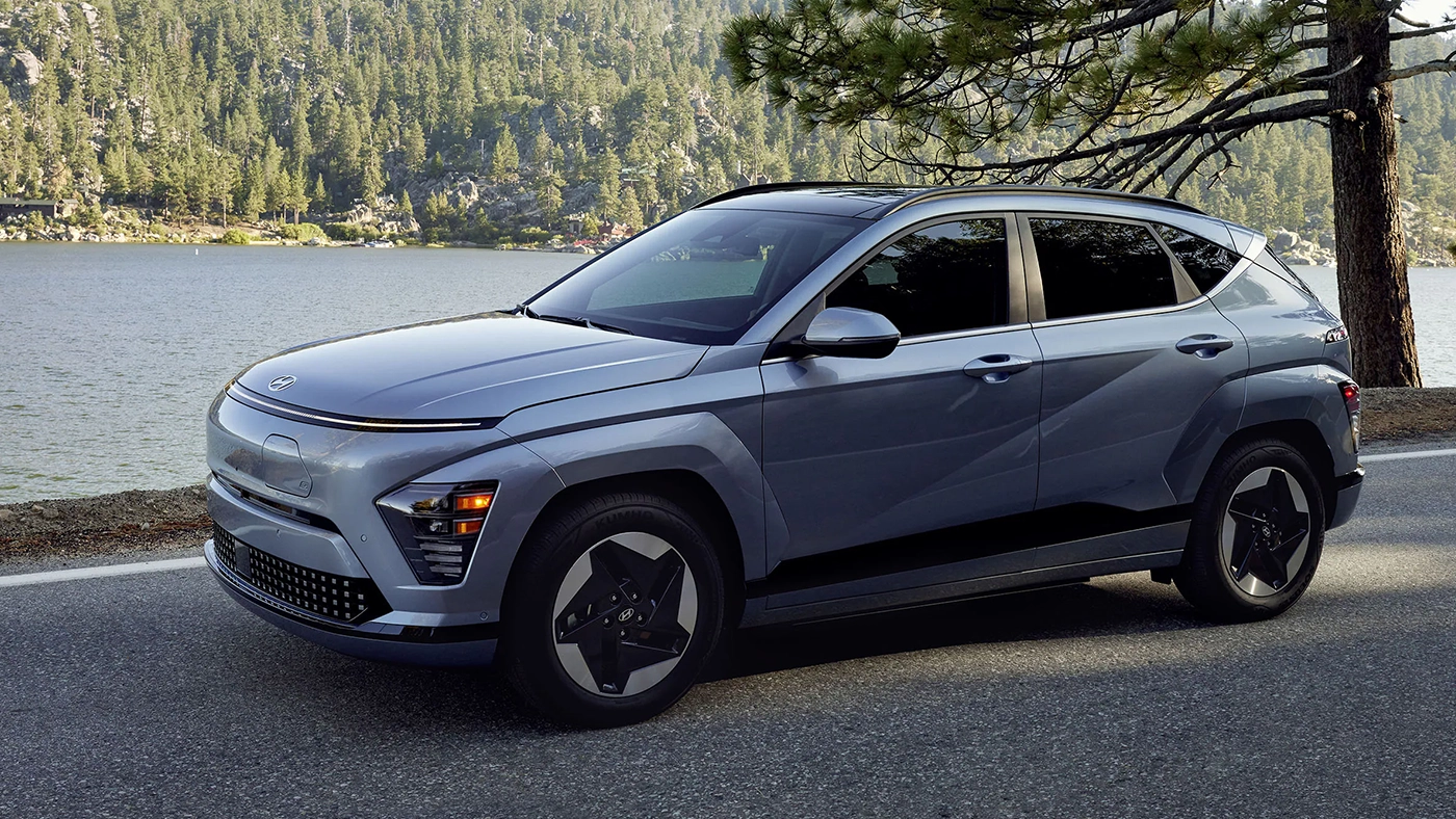 Three-quarter front and side view of the 2026 Hyundai Kona EV parked at the roadside with a view of the lake